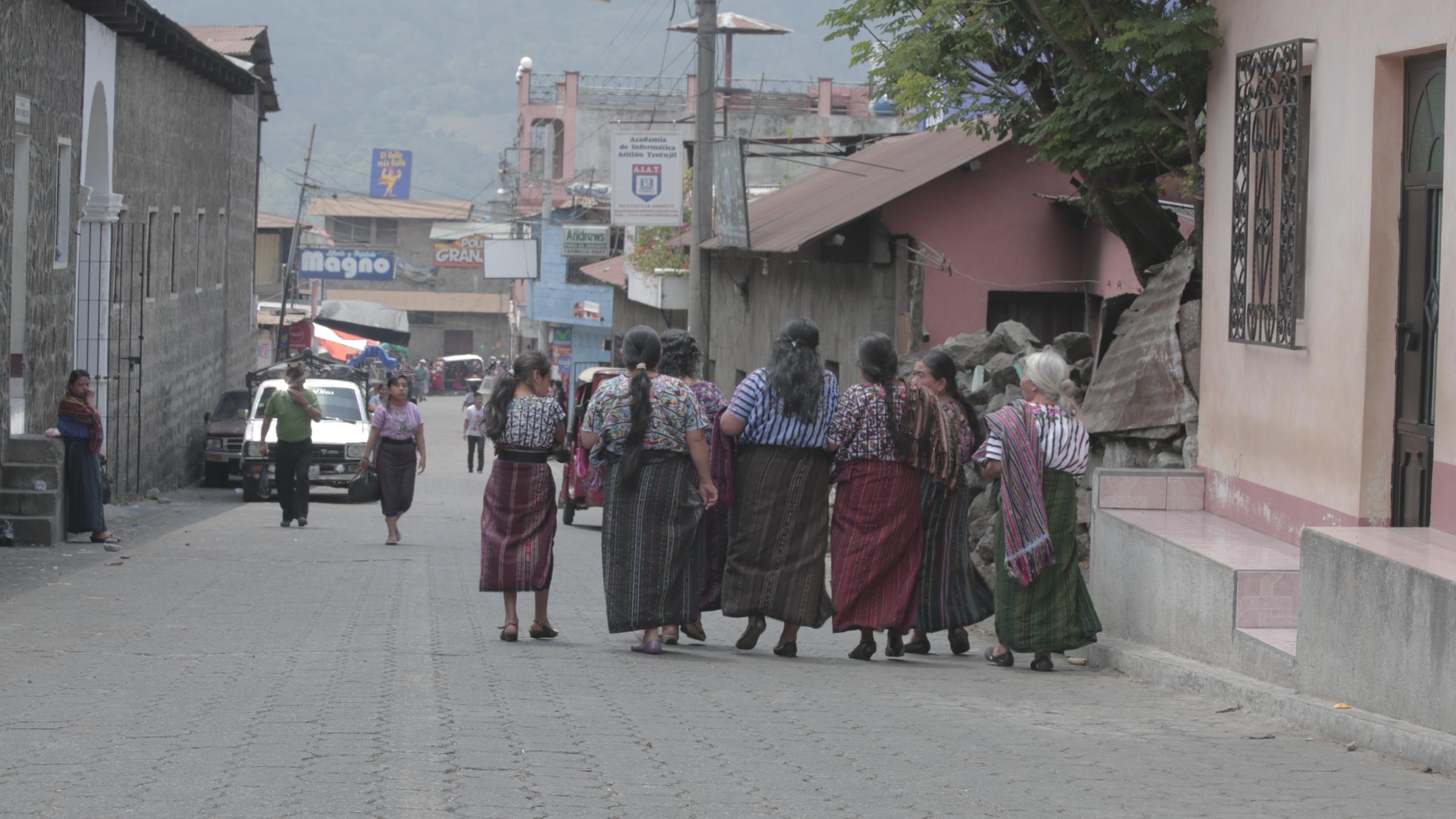 Women in traditional dress walk arm in arm down a town street
