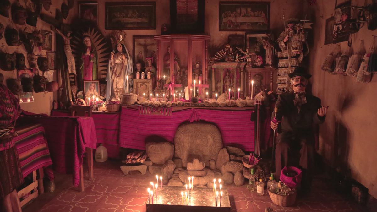 A candlelit altar crowded with saints, offerings and carved stones