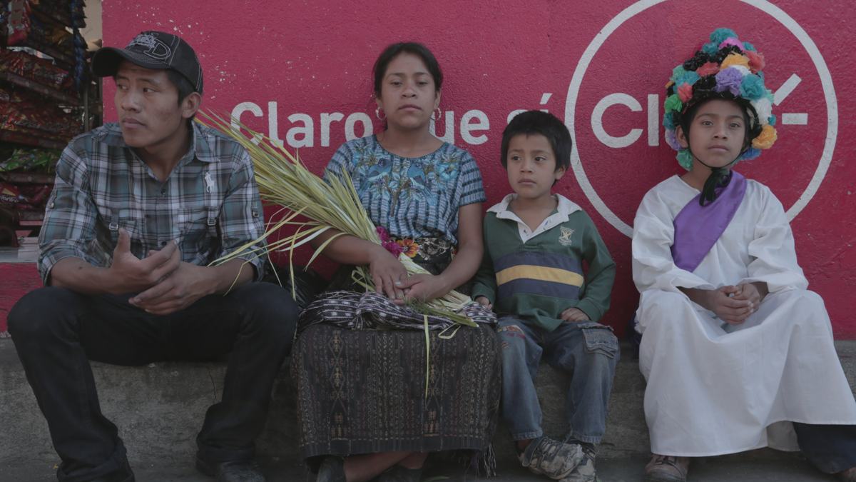 A family sits on a curb in front of a bright red advertising wall