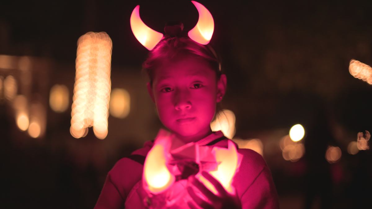 A girl in glowing horns holds a candle at night