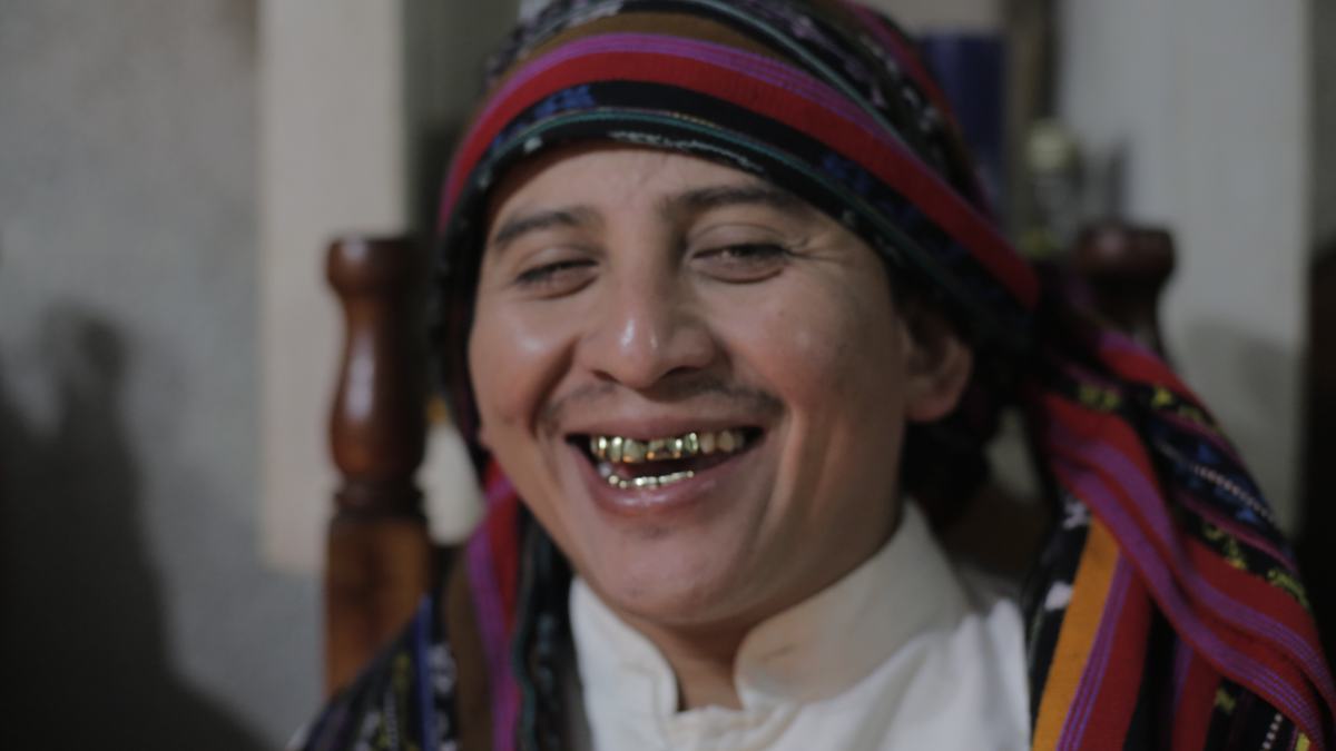 A man in a striped headwrap laughs, gold teeth catching the light