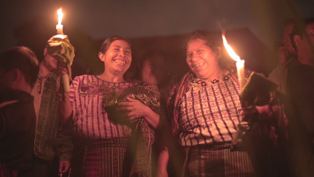 Two women laugh while holding candles at a night gathering
